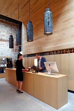 two people are standing at the front desk of a coffee shop, one is typing on her laptop