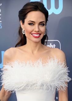 a woman in a white dress with feathers on her shoulders and chest, smiling at the camera