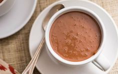 a cup of hot chocolate on a saucer next to a plate with spoons