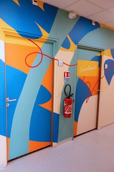 two blue and yellow doors with red handles in front of a wall painted with an abstract design