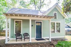 two chairs are sitting in front of a small blue house with white trim on the porch