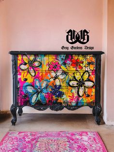 a colorful dresser with flowers painted on the front and sides, next to a pink rug