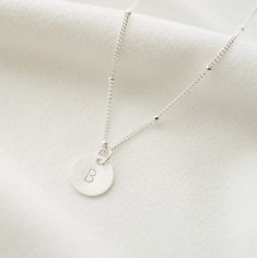 "A dainty silver coin is delicately suspended on a sterling silver necklace chain, and hand stamped with an uppercase letter of your choice. Add on additional coins personalized with letters of your choice, or a heart symbol. Hand stamped to order in our Vancouver studio. *Free shipping for orders to USA and Canada, and no duties or customs fees.* > Sterling silver coin is 9mm in diameter > Shown worn on a 16\" satellite chain > Comes beautifully packaged and ready for gift giving > Silver Minimalist Personalized Initial Necklace, Dainty Hand Stamped Round Disc Necklace, Dainty Hand Stamped Round Disc Necklaces, Minimalist Hand Stamped Sterling Silver Necklaces, Silver Engraved Dainty Coin Necklace, Dainty Sterling Silver Initial Necklace For Everyday, Dainty Engraved Silver Coin Necklace, Delicate Silver Pendant Initial Necklace, Everyday Hand Stamped Sterling Silver Necklaces