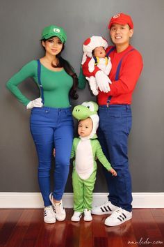 a family dressed up as mario and luigi the frog with their baby in front of a gray wall