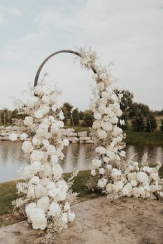 a wedding arch decorated with white flowers by the water