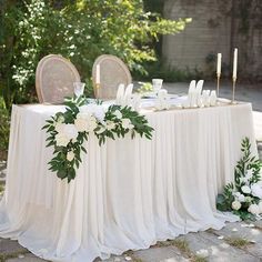 the table is set with white flowers and greenery