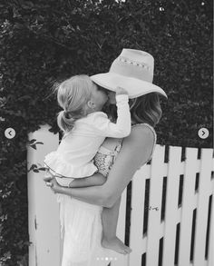 a woman holding a baby in her arms and kissing it's face while wearing a cowboy hat