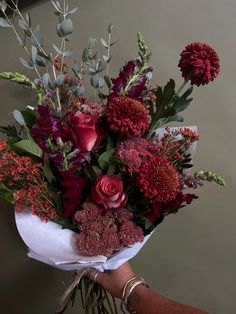 a bouquet of flowers is being held by someone's hand in front of a wall