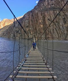 two people walking across a suspension bridge over water