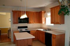 an empty kitchen with wooden cabinets and black appliances in the center, along with white counter tops