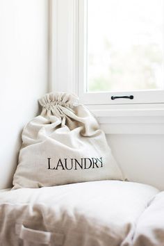 a white laundry bag sitting on top of a bed next to a window with the word laundry written on it