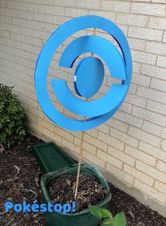 a blue sculpture sitting on top of a green planter next to a brick wall