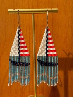 a pair of beaded sailboats are hanging from a hook on a wooden stand