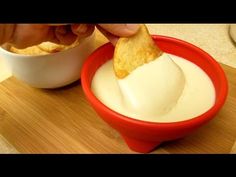 a person dipping some kind of food into a red bowl on top of a wooden cutting board