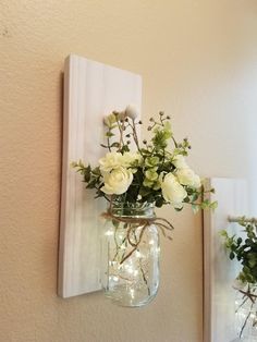 two mason jars with flowers in them are hanging on the wall next to a mirror