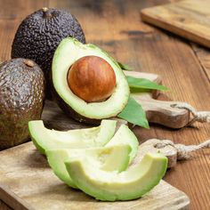 an avocado cut in half sitting on a cutting board next to other fruits