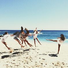 four girls jumping in the air on a beach with blue water and sky behind them