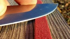 a person holding a knife on top of a wooden table next to red and blue strips