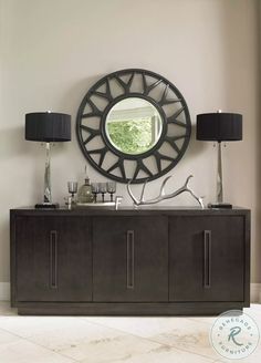 a large round mirror on the wall above a sideboard with two lamps and a lamp