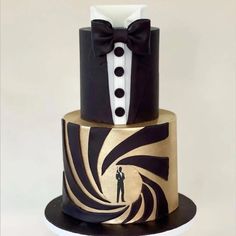 a three tiered cake decorated with black and gold designs, two men in tuxedos