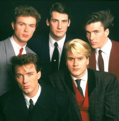 four young men in suits and ties posing for a photo together with one man looking at the camera