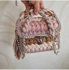 a hand holding a pink and white purse with chains hanging from it's handle