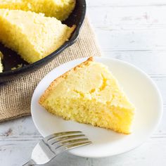 a piece of cake on a white plate with a fork next to it and a skillet in the background