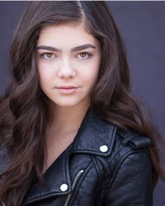 a woman with long brown hair wearing a black leather jacket and looking at the camera