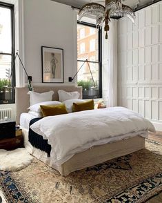 a large white bed sitting in the middle of a bedroom next to a tall window