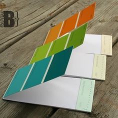 three different colors of paper sitting on top of a wooden table next to each other