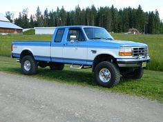 a blue and white pickup truck parked on the side of a road in front of a barn