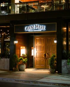 an entrance to a restaurant at night with lights on and potted plants in front