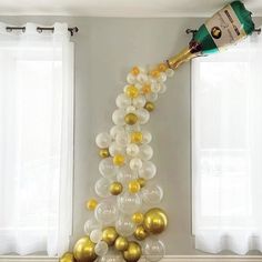 a champagne bottle is pouring into some balloons in the shape of a christmas tree with gold and white balls