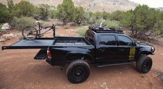 a black truck parked on top of a dirt road next to a bike rack and trees