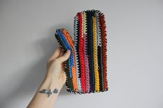 a hand is holding up some colorful crocheted hairbrushes on a white wall