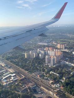 an airplane wing flying over a city with tall buildings and lots of trees on the other side