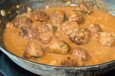 meatballs and gravy are being cooked in a skillet on the stove