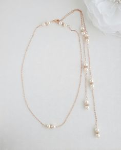 two necklaces with pearls on them sitting next to a white flower and a rose