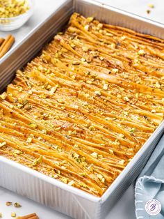 a casserole dish filled with baked goods on a white table next to cinnamon sticks