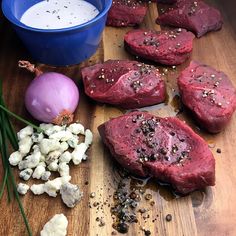 raw meat and vegetables on a wooden cutting board next to a blue bowl with milk