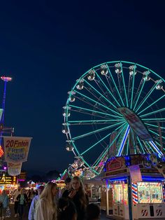 people are standing in front of a ferris wheel at an amusement park during the night