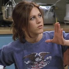 a woman sitting at a table with her hands in the air and an american eagle t - shirt on