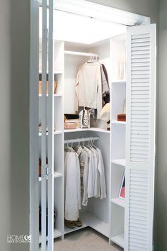 an open closet with clothes hanging on shelves and white shutters, in front of a window