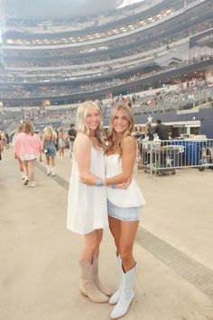 two women standing next to each other in front of a crowd at a baseball game