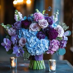 a vase filled with purple and blue flowers sitting on top of a table next to two candles