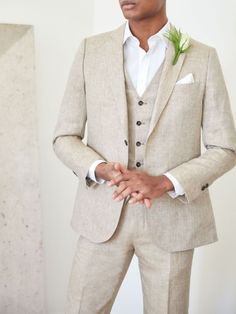 a man in a tan suit and white shirt with a flower on his lapel