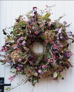 a wreath hanging on the side of a white building with purple flowers and green leaves