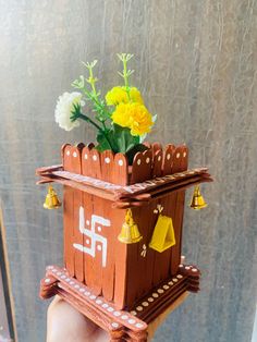 a hand holding up a small wooden house with flowers in the roof and bells on it