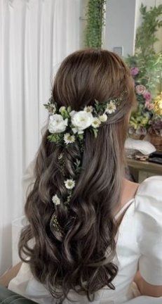 a woman with long hair and flowers in her hair sitting on a chair next to a window