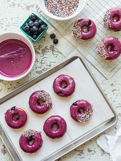 doughnuts with sprinkles and blueberries are on a tray next to bowls of fruit